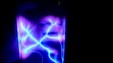 Karanlığın içindeki makro el görüntüsü içinde kıvrımlı neon ışınları olan bir elektrik lambasını tutuyor.