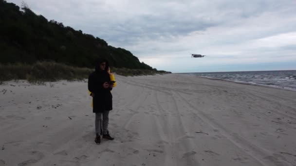 Kadın ve erkek, kumsalda okyanusun yanında duruyor ve insansız hava aracını ağır çekimde uçuruyorlar. — Stok video