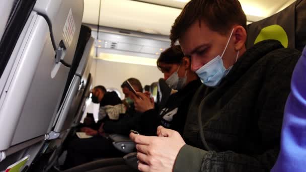 Las personas con máscaras médicas están sentadas en la tabla del avión y usando teléfonos inteligentes — Vídeos de Stock