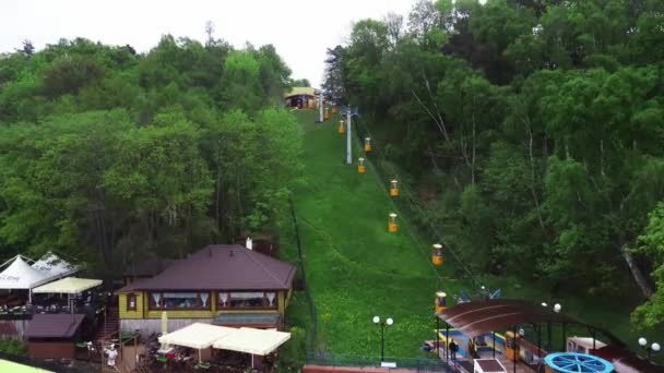 Funicular moving on the peak of a mountain among green trees at summer day is filmed by drone — Stock Video