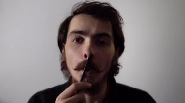 Genç adam sakalını tarıyor ve beyaz arka planda izole edilmiş kameraya bakıyor.