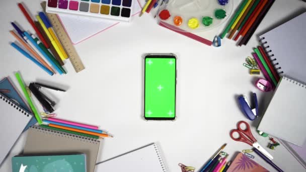 Ensemble de 26 gestes sur l'écran vert du smartphone couché sur la table blanche parmi les accessoires scolaires — Video