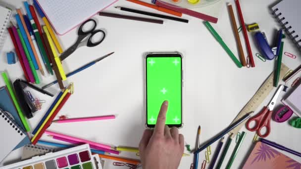 Состав школьных аксессуаров, окружающих смартфон с зеленым экраном и человеческим нажимом на дисплее — стоковое видео