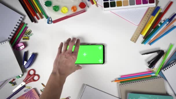 Man put smartphone with chroma key in horizontal orientation on the table full of school supplies — Stock Video