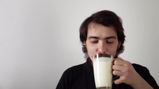 Retrato isolado de jovem barbudo bebendo kefir do vidro e sorrindo no fundo branco — Vídeo de Stock