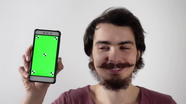 Smiling man holds smartphone with green screen and tracking markers and show on it — Stock Video