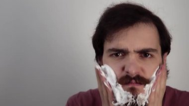 Kaba adam yanaklarına köpük sürüyor ve kaşlarını çatarak baltanın sakalını tıraş ediyor.