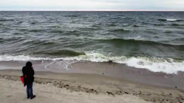 Чоловік стоїть на березі і дивиться на штормовий океан з величезними хвилями, знятими безпілотником — стокове відео