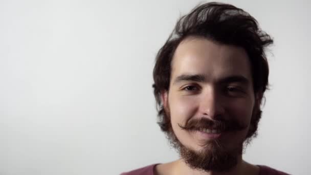 Ізольований портрет молодого бородатого чоловіка, який знімає окуляри, потім погладжує волосся і посміхається — стокове відео