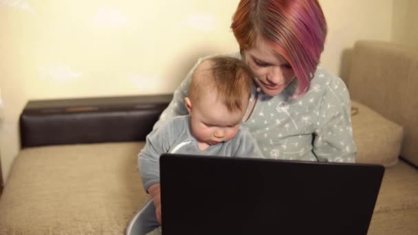 Мама работает из дома сидя перед ноутбуком с маленьким сыном на коленях — стоковое видео