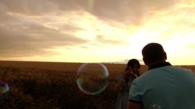 Erkek ve kadın gün batımında buğday tarlasında sabun köpüğü üflüyorlar.