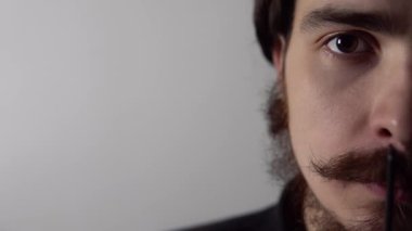 Sakalını ve bıyığını beyaz arka planda tarayan genç bir adamın izole edilmiş portresi.