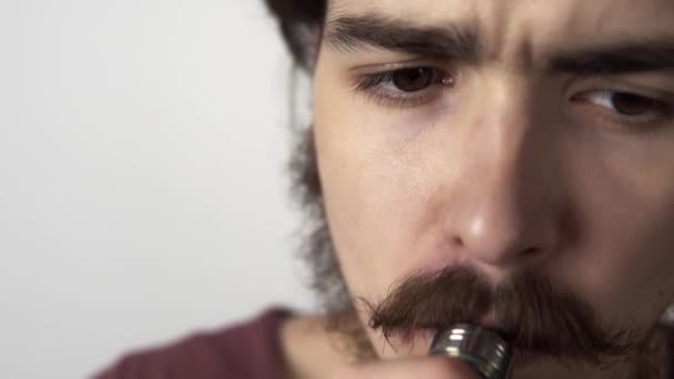 Primo piano filmato di giovane uomo serio barbuto fumare vaporizzare su uno sfondo bianco — Video Stock