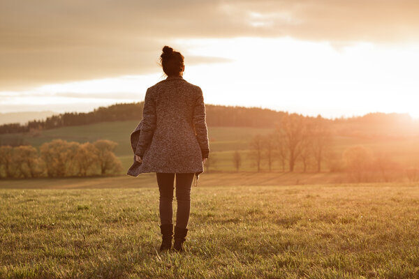 girl is standing on the meadow and watching the sunset