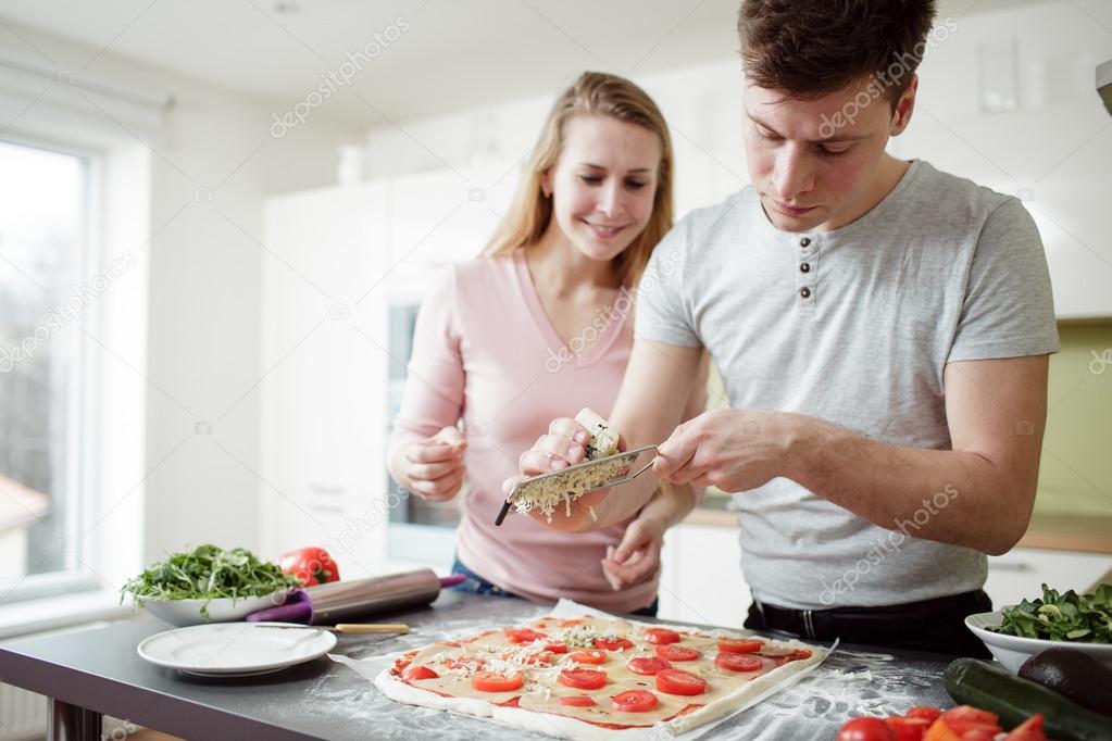 man is grating cheese on the pizza