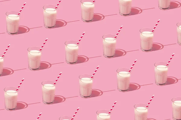 Creative pattern made with glass of milk and red and white paper straw on pastel pink background. Retro aesthetic style. Minimal creative concept.