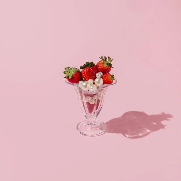 Creative concept with strawberries, white pearls  and glass jar on pastel pink background. Minimal fruit or food layout. Romantic spring idea.
