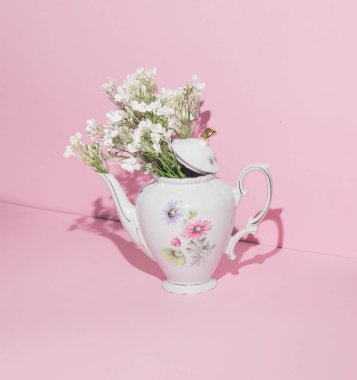 Pastel pembe arka planda beyaz bahar çiçekleri olan çaydanlık. Bahar sezonu yaratıcı fikri. Asgari retro çay zamanı konsepti.