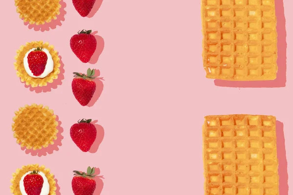 Creative pattern or frame made with strawberries and waffles on pastel pink background. Happy and fun breakfast or brunch idea with fruits. Flat lay.Strawberry fruit concept.