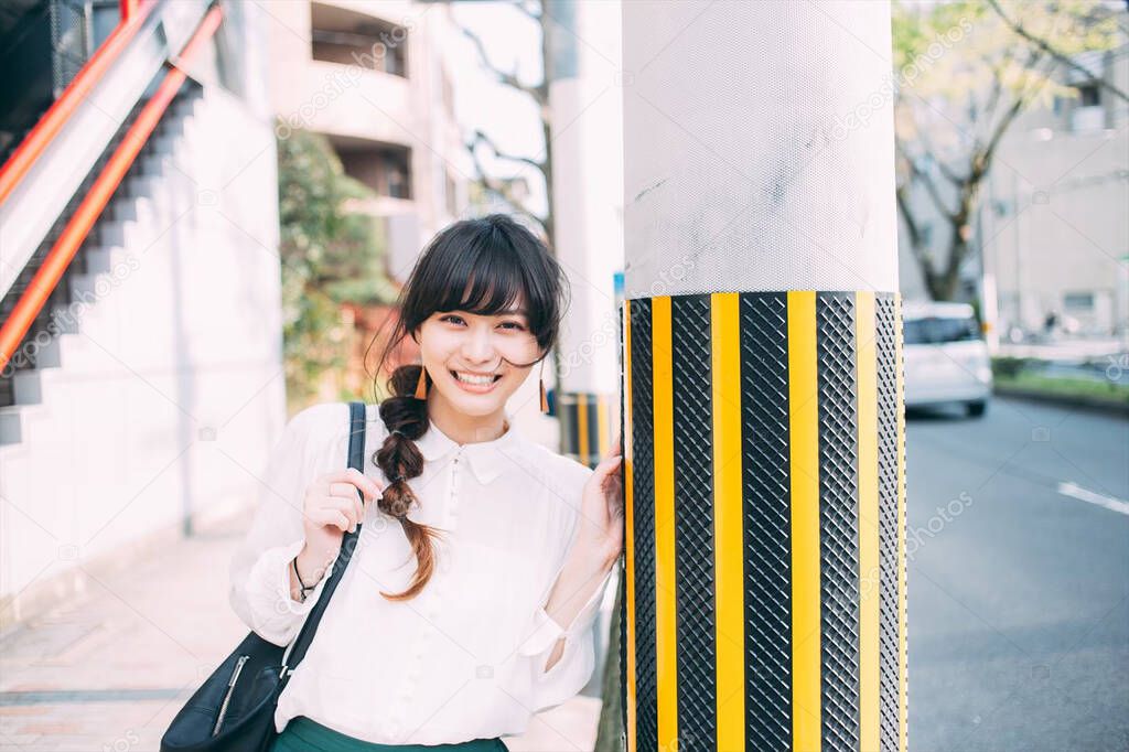 A Japanese woman with a beautiful smile strolling along a street corner and an electric pole.