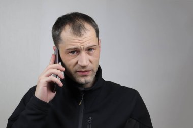 Kafkasyalı genç bir adam akıllı bir telefonla konuşuyor. Kötü haberler aldı. Seçici odaklanma. Gri arkaplan.