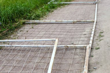 Metal, eski, kirli parmaklıklar yolda tellerle bağlanmış çimenlerin arasında, yerde yatıyordu.