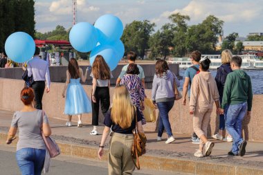 İnsanlar güneşli bir yaz gününde doğal granit kıyıları olan bir nehir kıyısında büyük bir Avrupa şehrinde yürürler. Bir kız ve genç bir adam büyük şişme mavi balonlar tutuyor. Bir gemi nehirde yüzüyor.