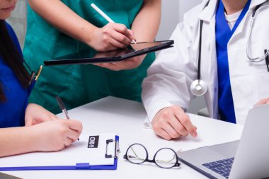 Üç doktor masada toplanıp notlar alıyorlar.