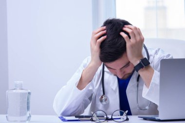 Doktor elleri başının üstünde masada oturuyordu.