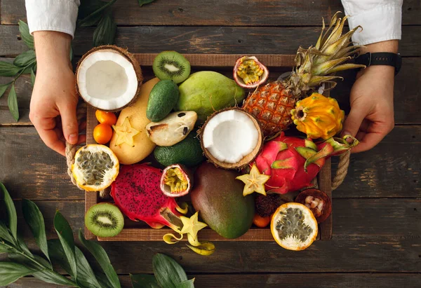 Adam elinde egzotik meyveler olan tahta bir tepsi tutuyor.