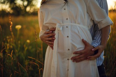 Bir adam ellerini hamile bir kadının karnına bastırıyor. Karı koca. Gün batımında bebek partisi. saf aşk. Aile. Göbekteki bebek