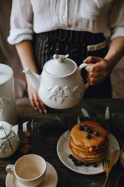 Seorang Wanita Memegang Ketel Teh Putih Dengan Sepiring Pancake Teko — Stok Foto