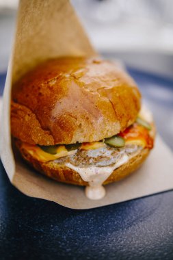 Siyah tabakta kahverengi kağıt içinde sulu bir burger.