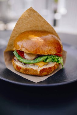 Siyah tabakta kahverengi kağıt içinde sulu bir burger.