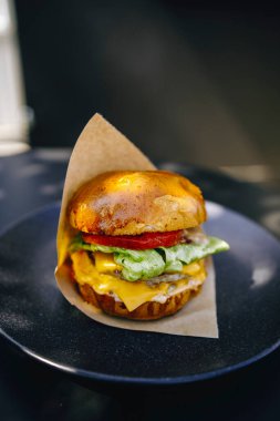 Siyah tabakta kahverengi kağıt içinde sulu bir burger.