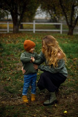 Genç bir kadın çiftlikte mutlu ve gülümseyen bir çocuğa sarılıyor. Mutlu çocuk bulutlu havada bahçede annesinin yanında duruyor. Anne ve oğlu sonbahar bahçesinde ya da parkta. kırsal yaşam tarzı