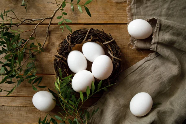 fresh white chicken eggs in a nest on a wooden background with green branches. Easter eggs.