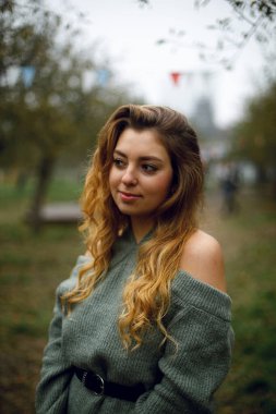 Kız rüya gibi dışarı bakıyor. Parktaki genç bir kadının portresi. Bahçede çıplak omuzları olan kazaklı güzel bir kız.