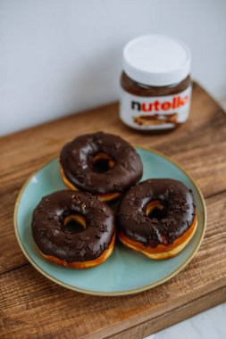 KYIV, UKRAINE - 1 Nisan 2021: Nutella kutusunun yanında üç çikolatalı çörek. Nutella çikolata ezmesiyle kaplanmış donutlar..