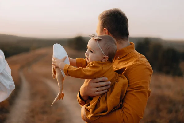 在爸爸怀里抱着他心爱的鲸鱼玩具的女婴 一个小孩子在他父亲的手里 傍晚时分 女儿和父亲在田里散步 — 图库照片