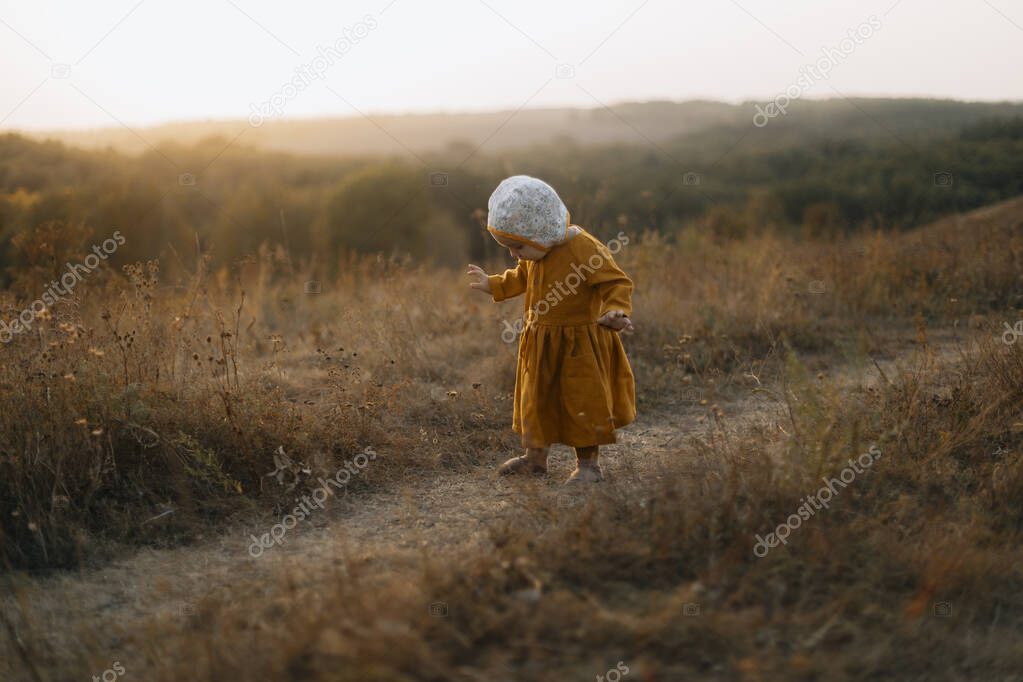 the child looks under his feet. baby walks along a path on a hill or mountain. little girl in a brown dress and hat. child and pure nature