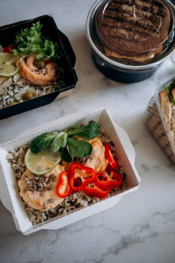 Tabaklar mermer yüzey manzaralı kağıt bir kabın içinde. Yemek teslimatı, yemek servisi ya da paket servis servisi. Kırmızı balık etli siyah ve kahverengi pirinç, hamburger. Sporcular için fitness yemeği