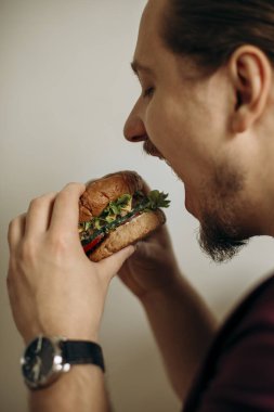 Aç adamın ellerinde taze, sulu bir burger. Adam taze bir hamburger ısırıyor. çoklu tahıllı taze hamburger..