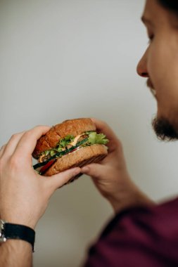 Sakallı bir gencin elinde bir hamburger. Aç bir adam çizburger yemeden önce onu tutar. Hamburger erkeklerin elinde, beyaz bir duvarın yanında..