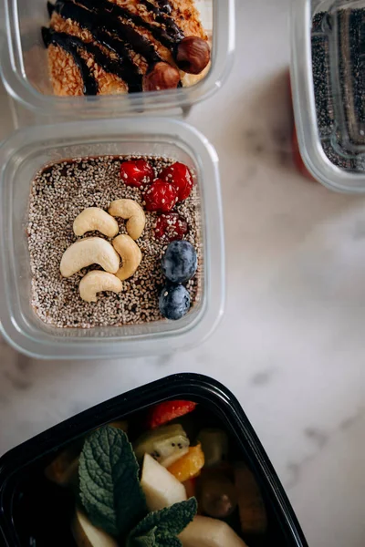 desserts in plastic containers on a marble surface top view. food delivery or catering food or takeaway food. chocolate mousse with chia, cashews and berries. fitness dessert for athletes