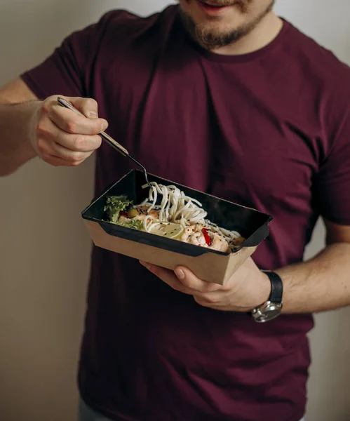 Neşeli mutlu adam yemek yiyecek. Aç adam yemek dağıtımından somon makarnası yiyor. Sağlıklı yemek teslimatı. somon sebzeli udon ve tohum..