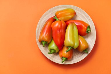 Renkli biber, turuncu arka planda, yazı alanı olan ahşap bir tabakta bir kaydırağın üzerinde yatıyor. Yukarıdan görünüşü.