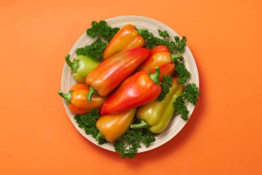 Renkli biber ve maydanoz, turuncu arka planda, tahta bir tabakta, yazı alanında bir kaydırağın üzerinde uzanıyor..
