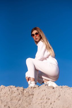 Güneşli bir günde kumların üzerinde beyaz elbiseler giymiş güzel, şık bir genç kadın.