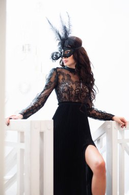 Güzel saç stili ve kırmızı dudaklı çekici esmer kadın, gece elbisesi içinde, şık aksesuarlı Venedik siyah maskesi.